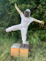 Girl beekeeper holding out arms while standing on top of beehive with green trees in the background.